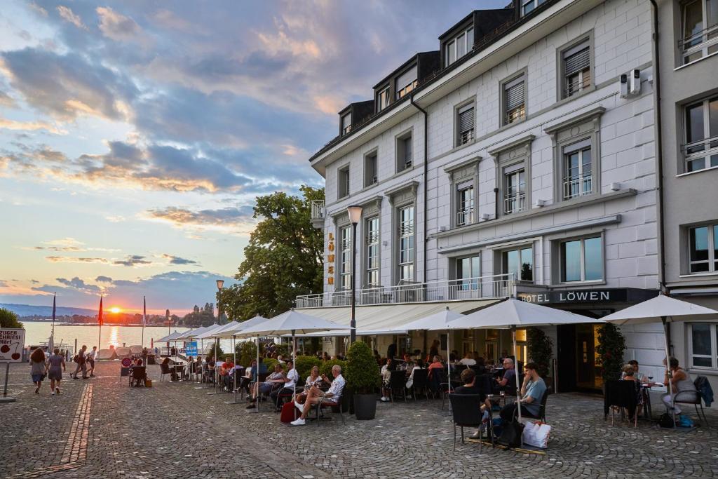 personas sentadas en mesas fuera de un edificio en Hotel Löwen am See, en Zug