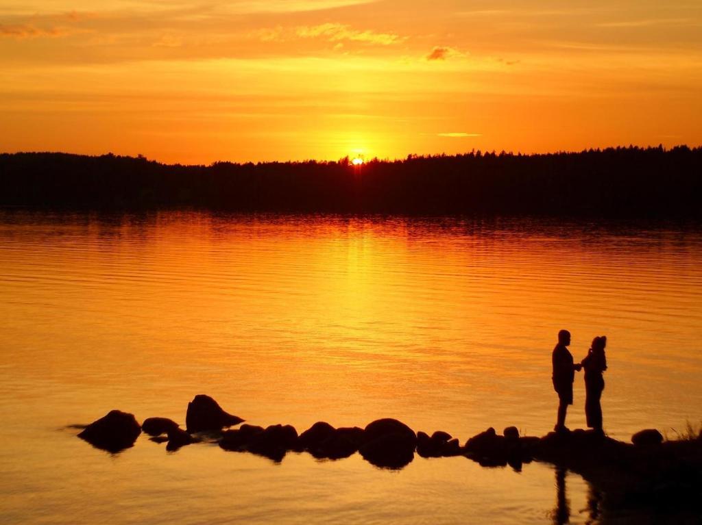 2 personnes debout sur la rive d'un lac au coucher du soleil dans l'établissement Koskenselkä Camping, à Puumala