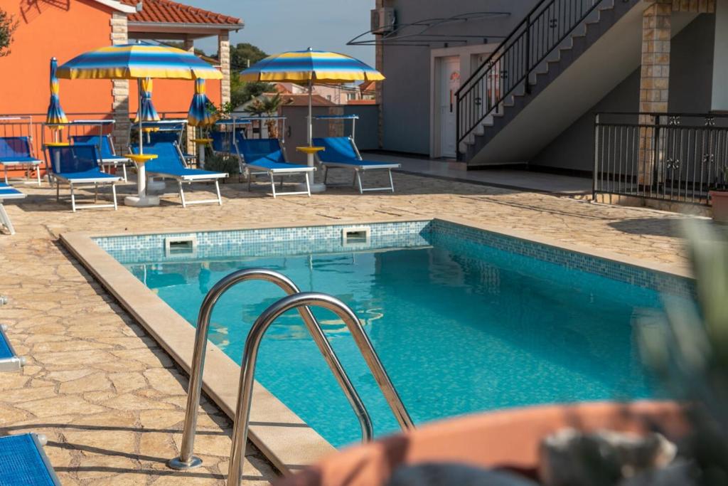 una piscina con sillas y sombrillas azules en Apartmani Grga, en Trogir