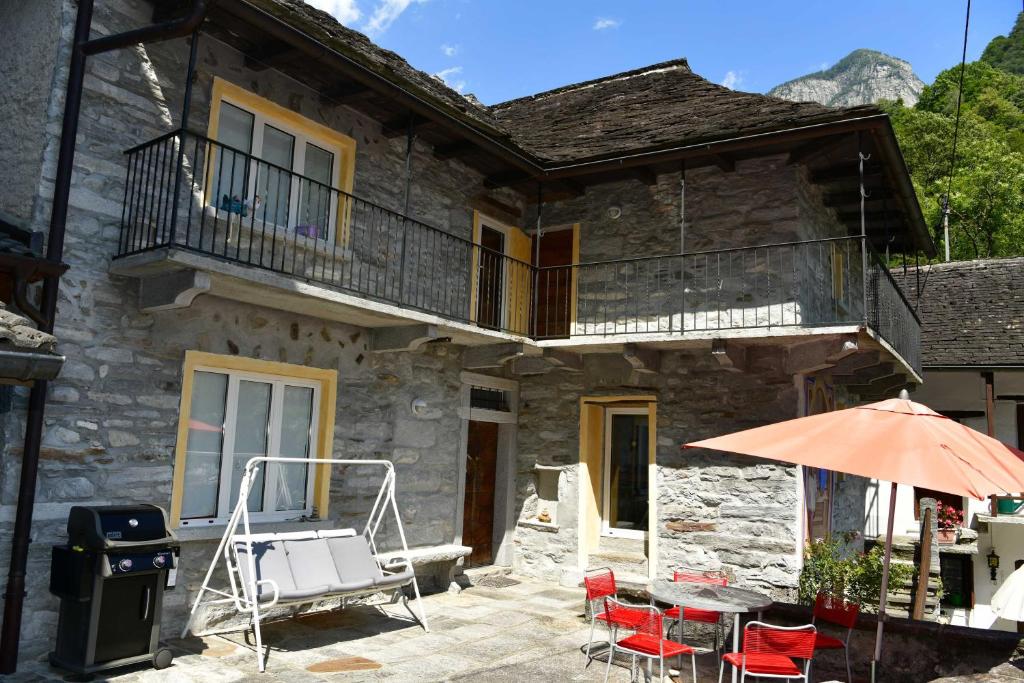 a stone house with a table and chairs and an umbrella at Rustico Luchessa Valle Verzasca in Lavertezzo