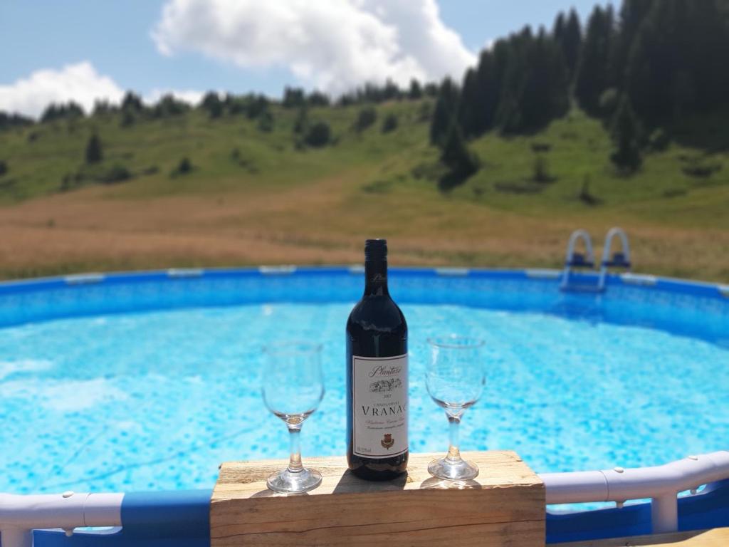 a bottle of wine and two wine glasses next to a swimming pool at Kamp Janketic in Kolašin