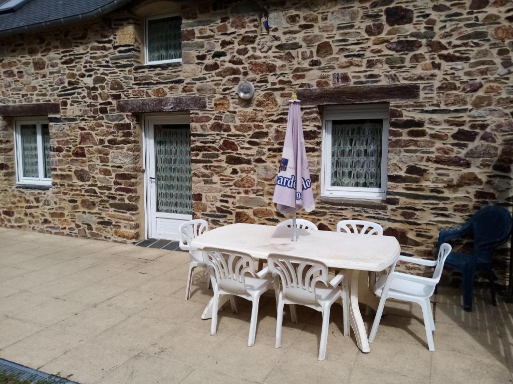 a white table and chairs with an umbrella in front of a building at Gîte la clef des garennes in Merléac
