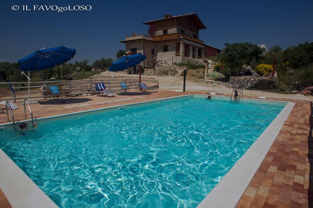 a swimming pool with blue umbrellas in front of a house at Il Favogoloso in Alatri
