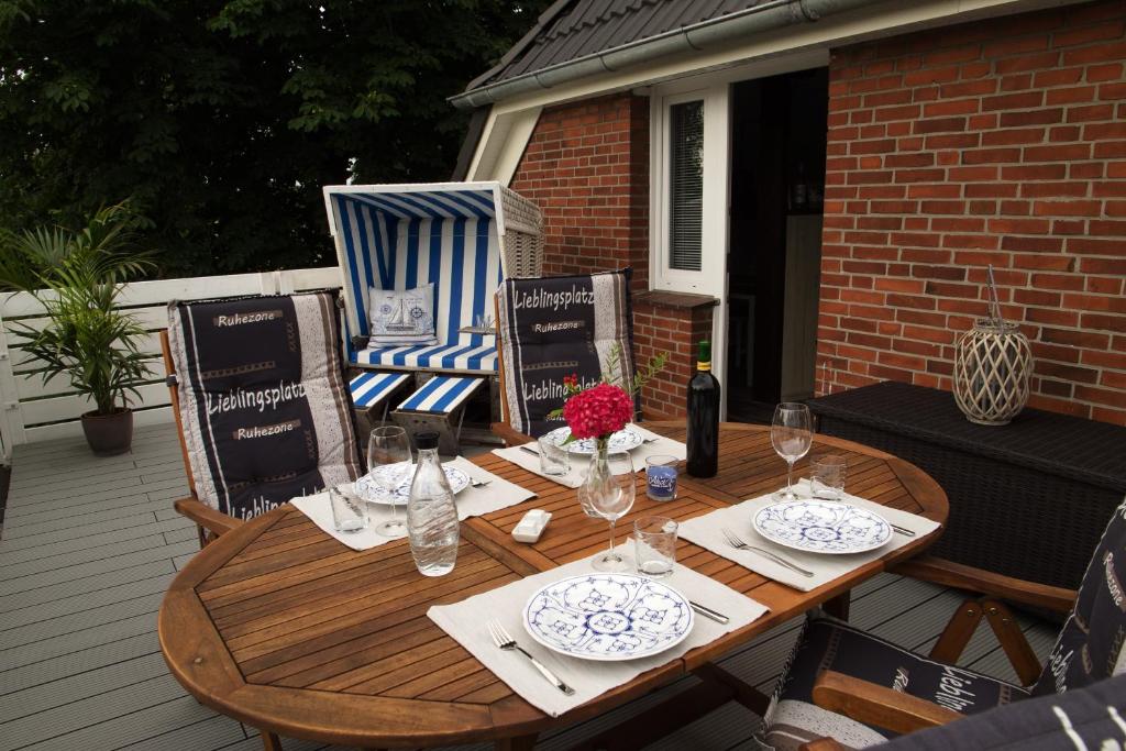 a wooden table with plates and wine glasses on a patio at Zur alten Post II in Dagebüll