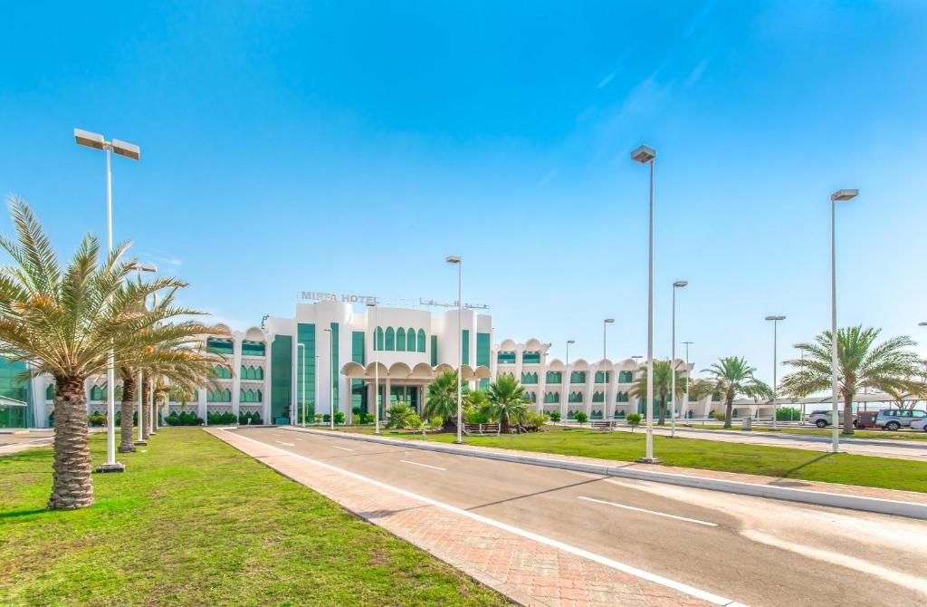 a road in front of a large building with palm trees at Mirfa Hotel in Al Mirfa
