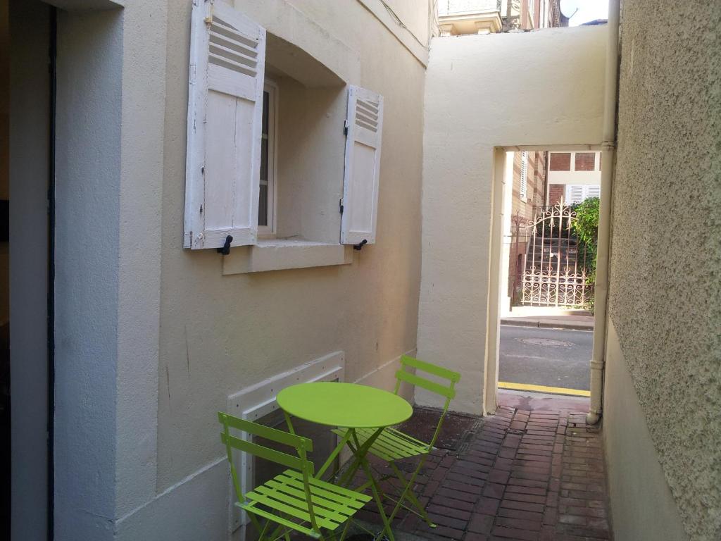une table et des chaises vertes sur le côté du bâtiment dans l'établissement Un chez soi bord de mer, à Trouville-sur-Mer
