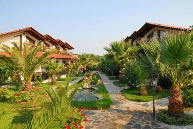 a resort yard with palm trees and flowers and houses at Oneiro Zois villas in Prinos