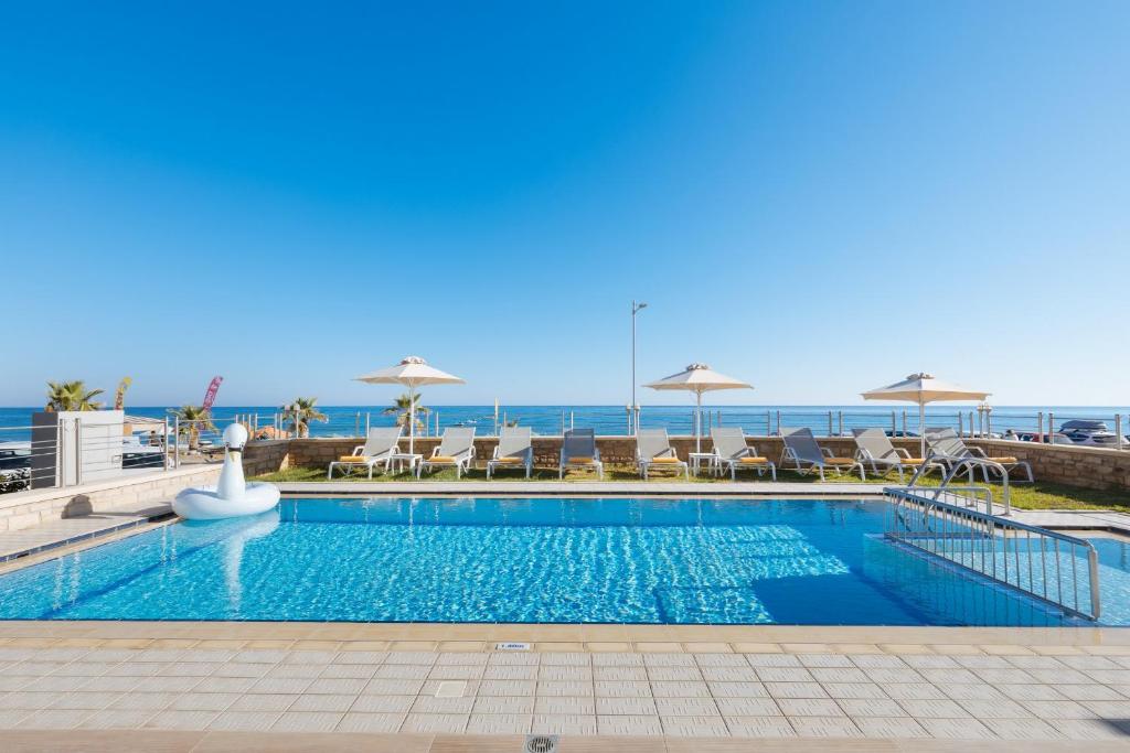 a swimming pool with chairs and umbrellas next to the ocean at Irida beachfront Villa for 12 steps to amenities in Rethymno