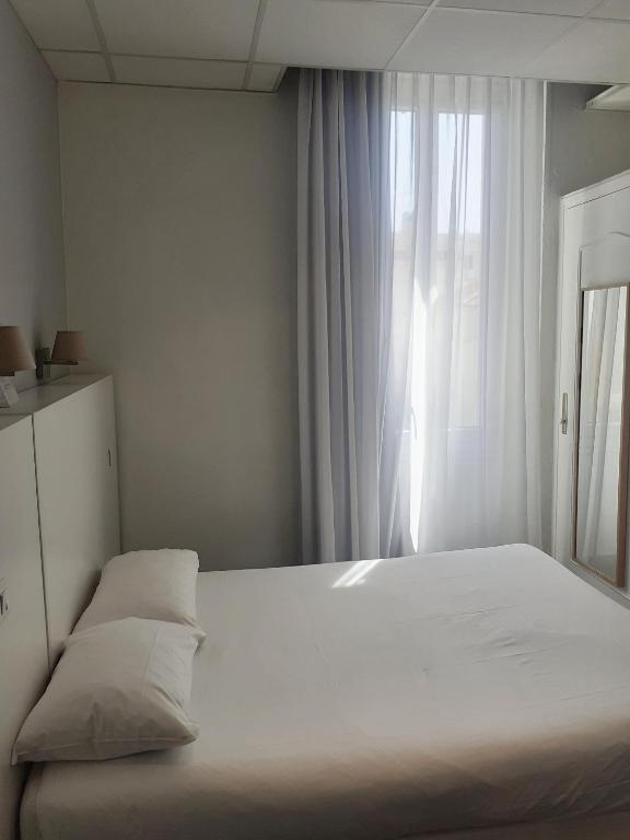 a bedroom with a large white bed with a window at Hôtel P.L.M. in Cannes