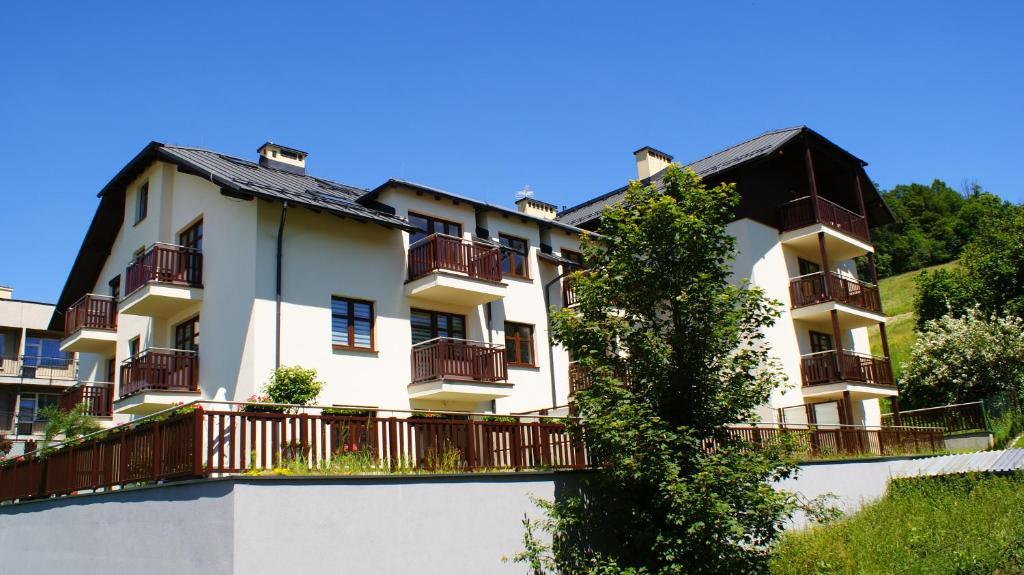 Un grand bâtiment blanc avec un balcon et un arbre est à votre disposition. dans l'établissement Apartamenty Willa Pogoń, à Krynica-Zdrój