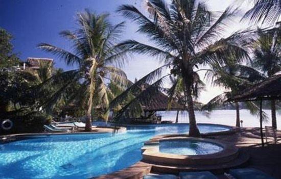 a swimming pool with palm trees next to the ocean at Tamarind Village Hotel Apartments in Mombasa