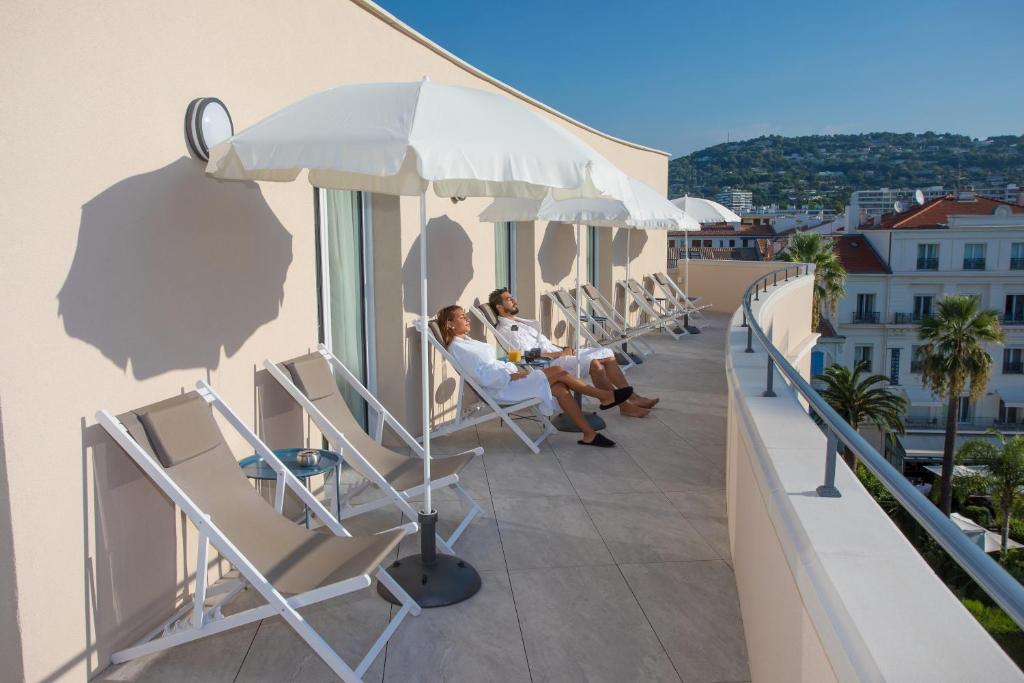 2 personnes assises sur le balcon d'un immeuble dans l'établissement Cristal Hôtel & Spa, à Cannes