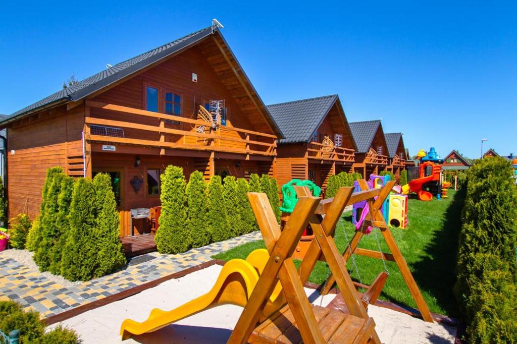 una casa de madera con un parque infantil delante de ella en Domki Kaper Karwia en Karwia