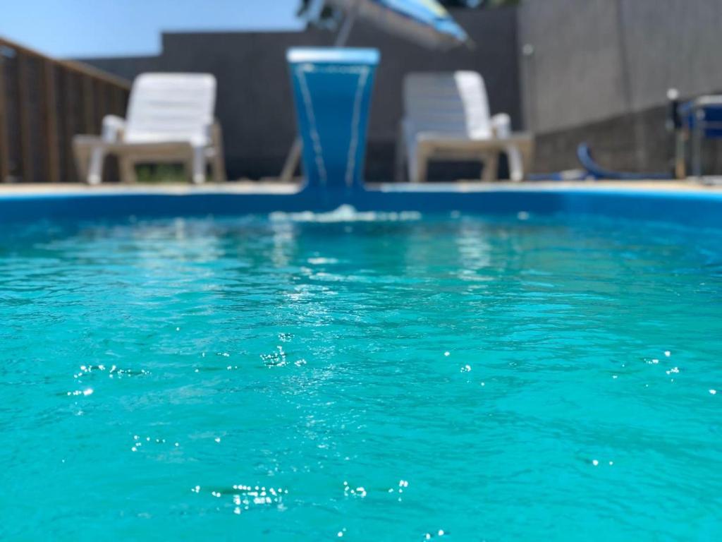 uma piscina com água azul e cadeiras brancas em Pousada Suítes do Rosa na Praia do Rosa