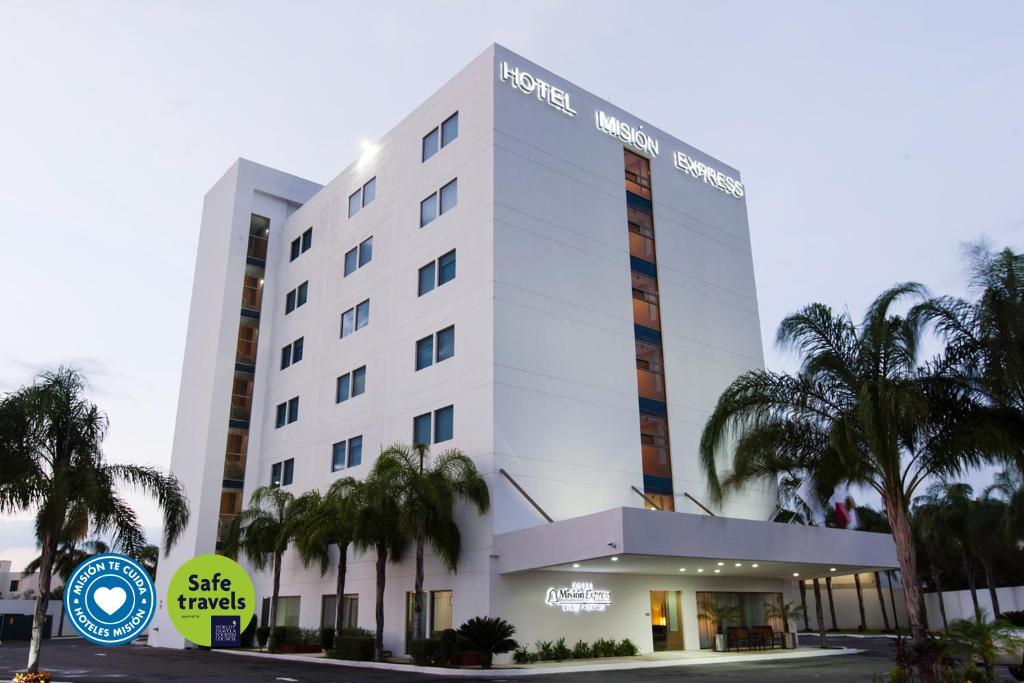 a white building with palm trees in front of it at Mision Express Merida Altabrisa in Mérida
