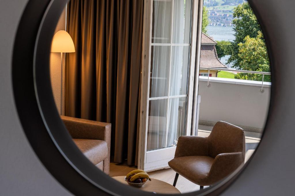 a mirror reflecting a room with two chairs and a window at Hotel Winkelried am See in Stansstad