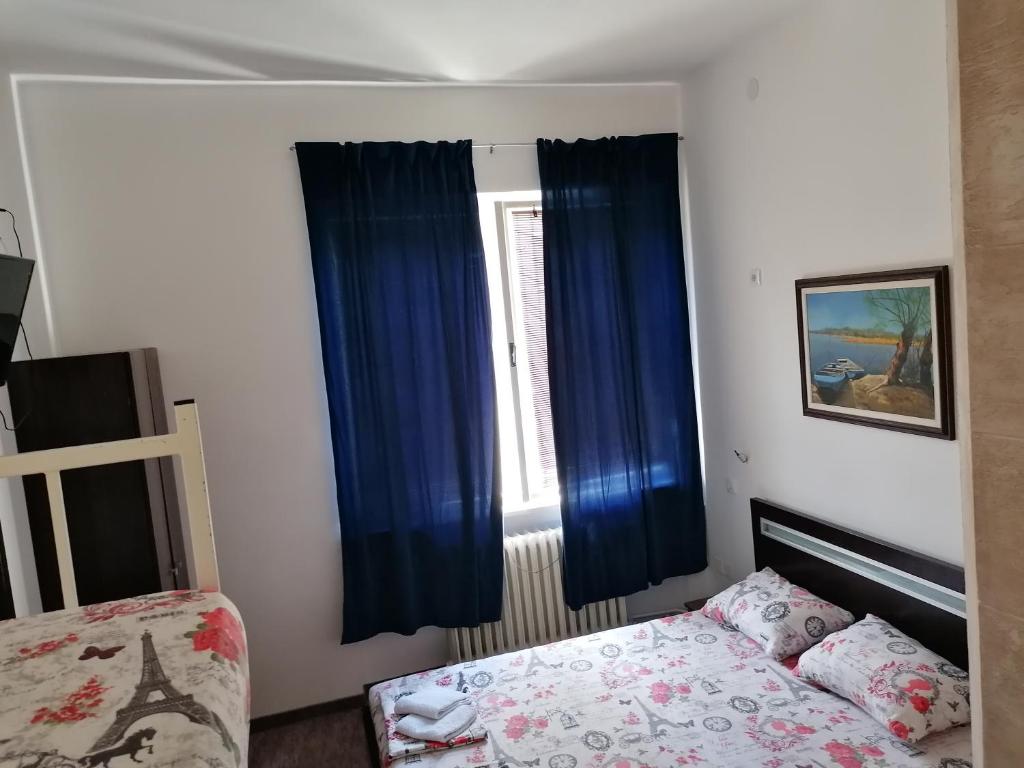 a bedroom with a bed and a window with blue curtains at Exit Labirint Centar in Novi Sad