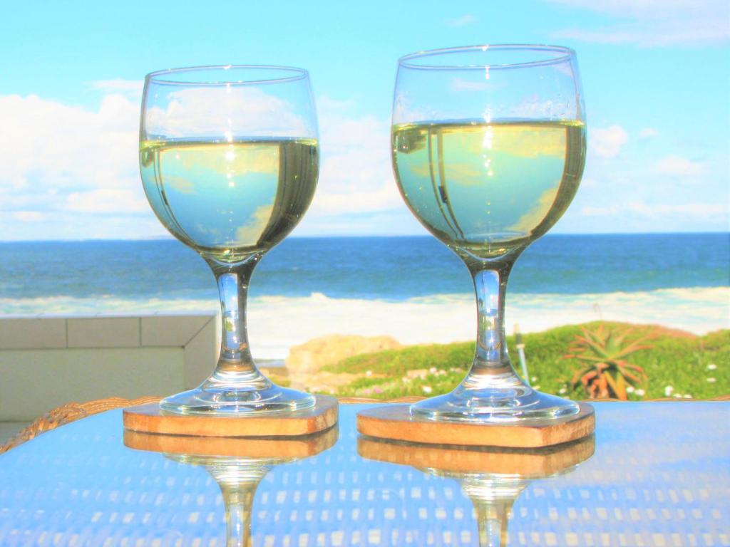 dos copas de vino sentadas en una mesa cerca del océano en Beachfront House - Hermanus Whale View en Hermanus