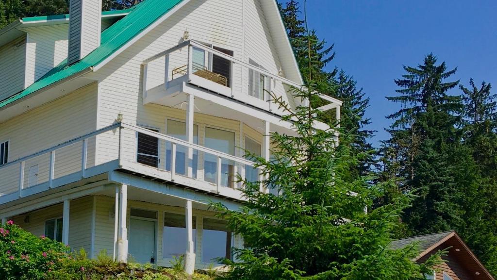 a white house with a balcony and a tree at Kelli Creek Cottage - REDUCED PRICE ON TOURS in Juneau