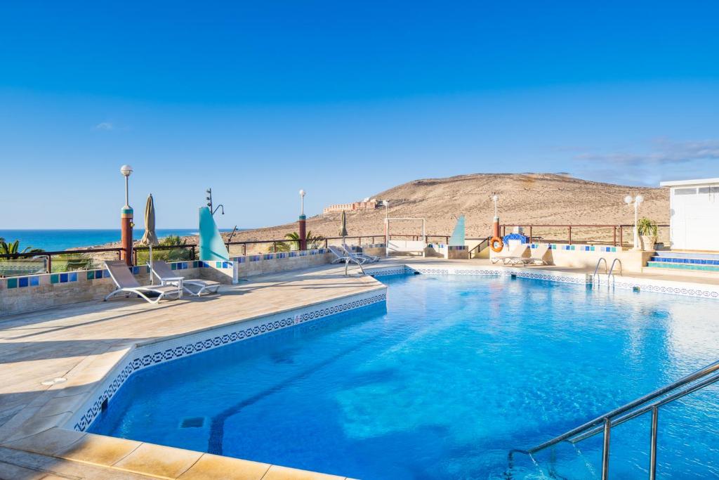 einen Pool mit Stühlen und das Meer im Hintergrund in der Unterkunft Hotel Esmeralda Maris by LIVVO in Costa Calma