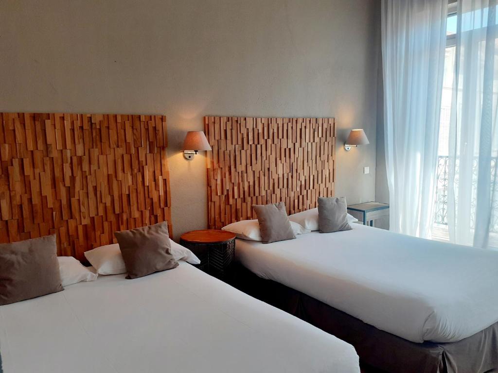 two beds in a hotel room next to a window at Hôtel La Villa Tosca in Cannes