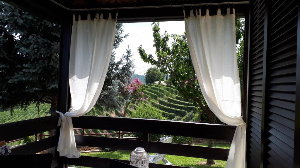 una finestra con tende bianche e vista sul giardino di Villa Edy Barbaresco a Barbaresco