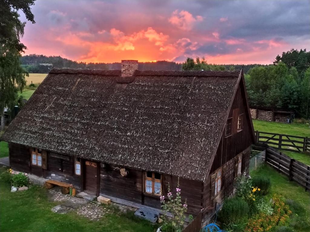 uma casa antiga com um telhado com um pôr-do-sol ao fundo em Kaszubska Zagroda em Lipuska Huta