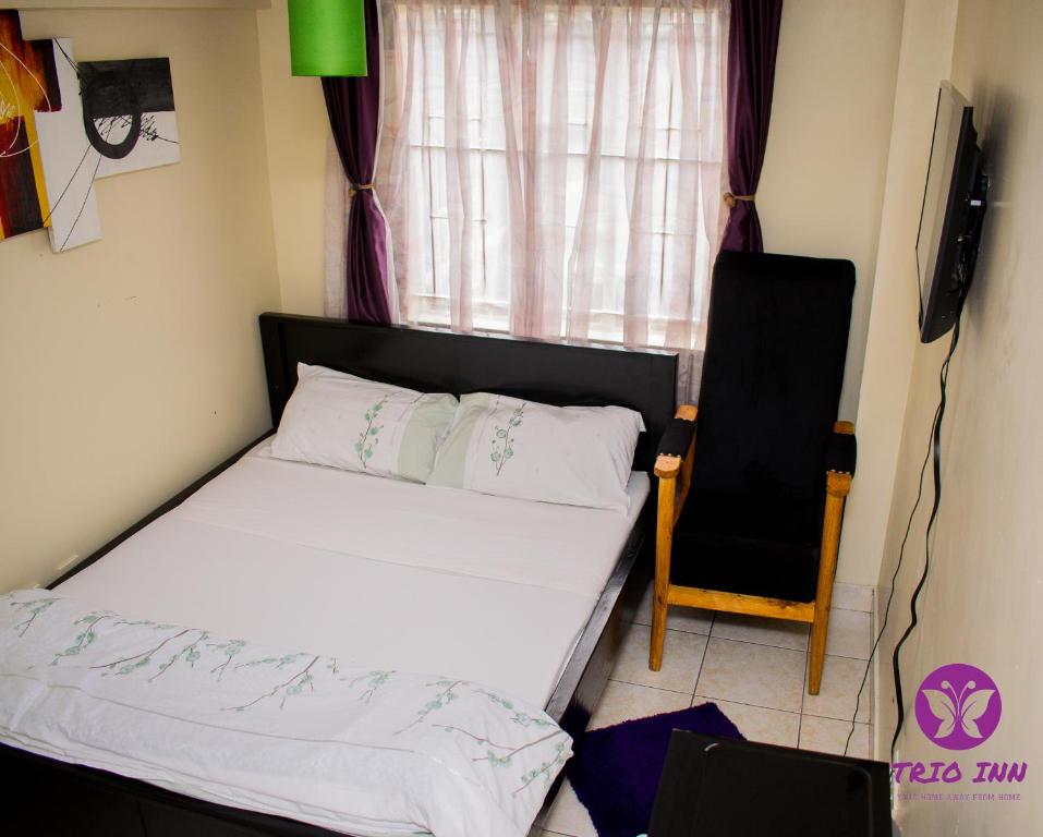 ein Schlafzimmer mit einem Bett, einem Stuhl und einem Fenster in der Unterkunft The Trio Inn in Nairobi