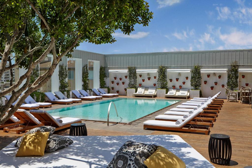 a pool with chairs, tables, and umbrellas in it at Mondrian Los Angeles in West Hollywood in Los Angeles