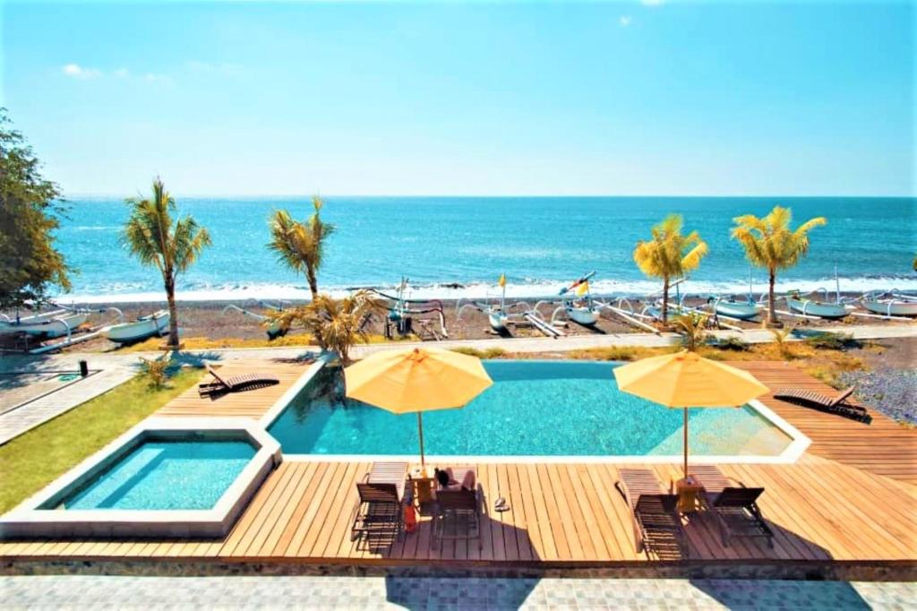 a swimming pool with chairs and umbrellas and the beach at Hi Blue Bali Melasti Resort in Karangasem