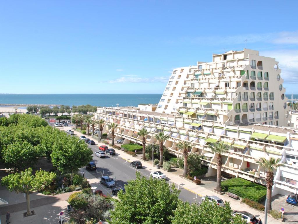 un grand bâtiment blanc avec des palmiers et l'océan dans l'établissement STUDIO 2-3 pers PARKING CLIM VUE PORT ET MER, à La Grande Motte