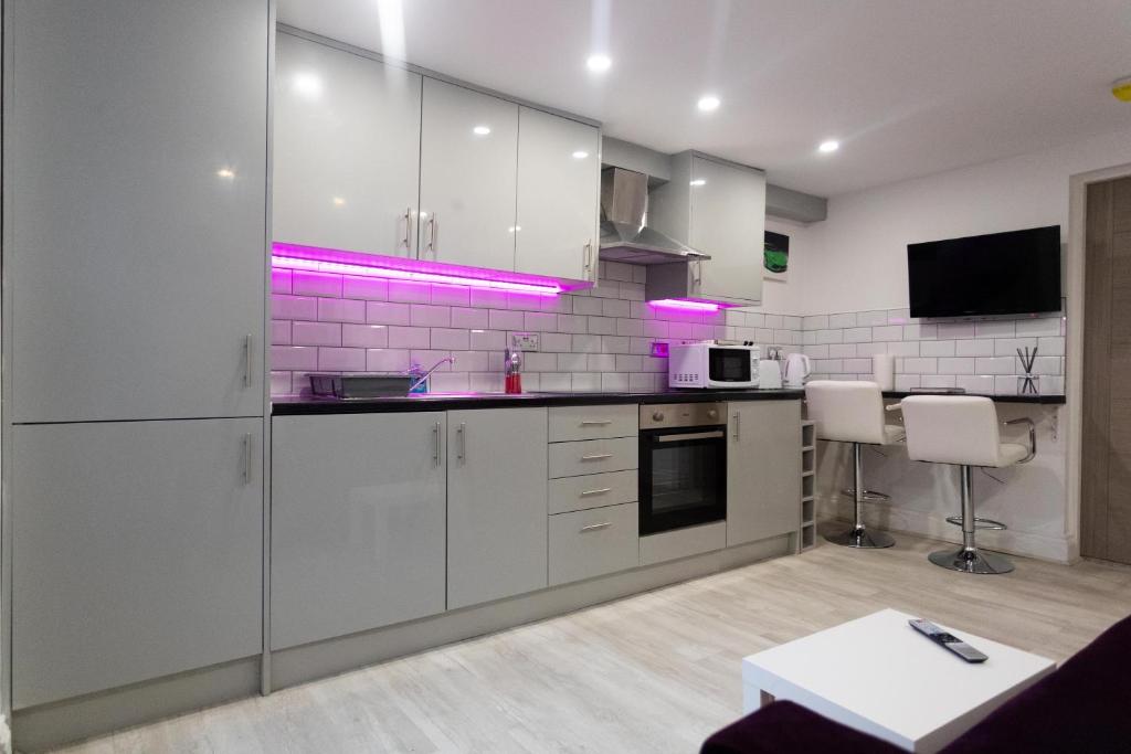 Westwood Apartment في ليدز: مطبخ مع خزائن بيضاء وأضواء أرجوانية