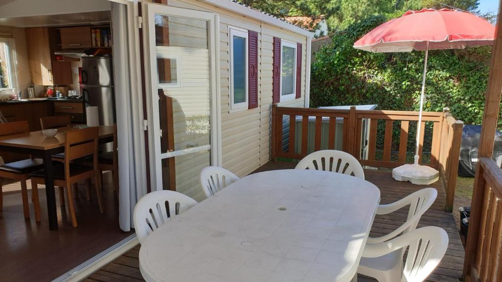 una mesa blanca y sillas en una terraza con sombrilla en Mobil-home Confort camping le bois Masson en Saint-Jean-de-Monts