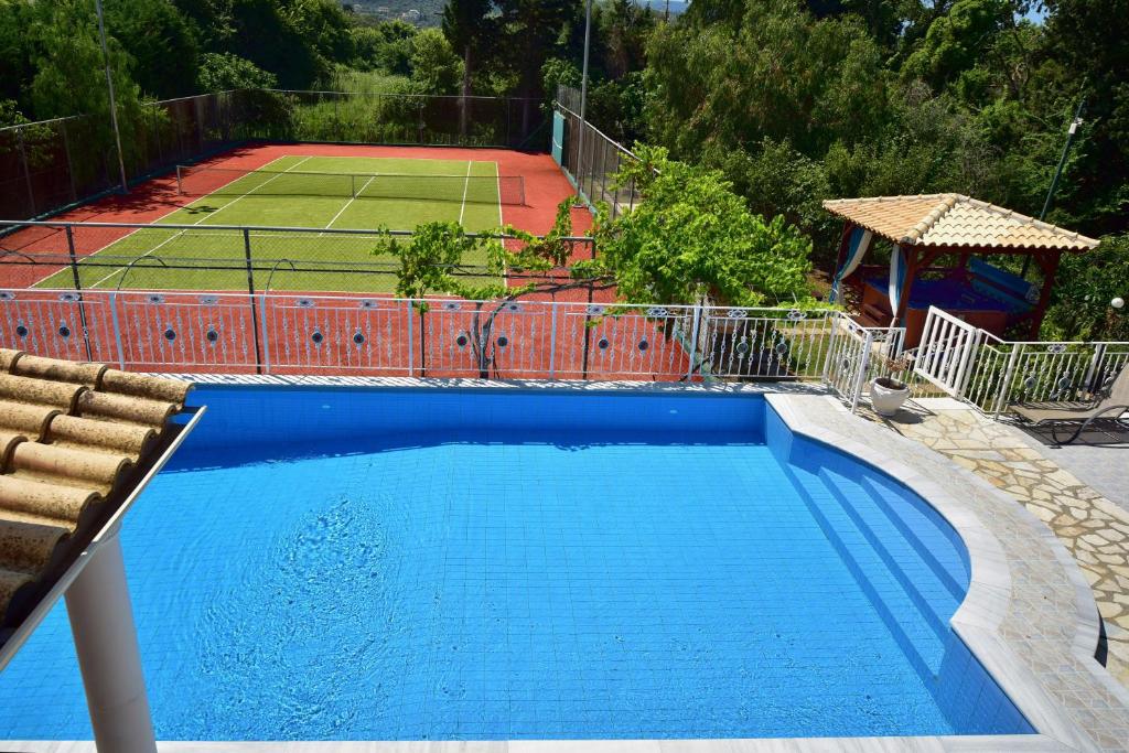 a large blue swimming pool with a tennis court at Villa Jolie Corfu Roda in Roda