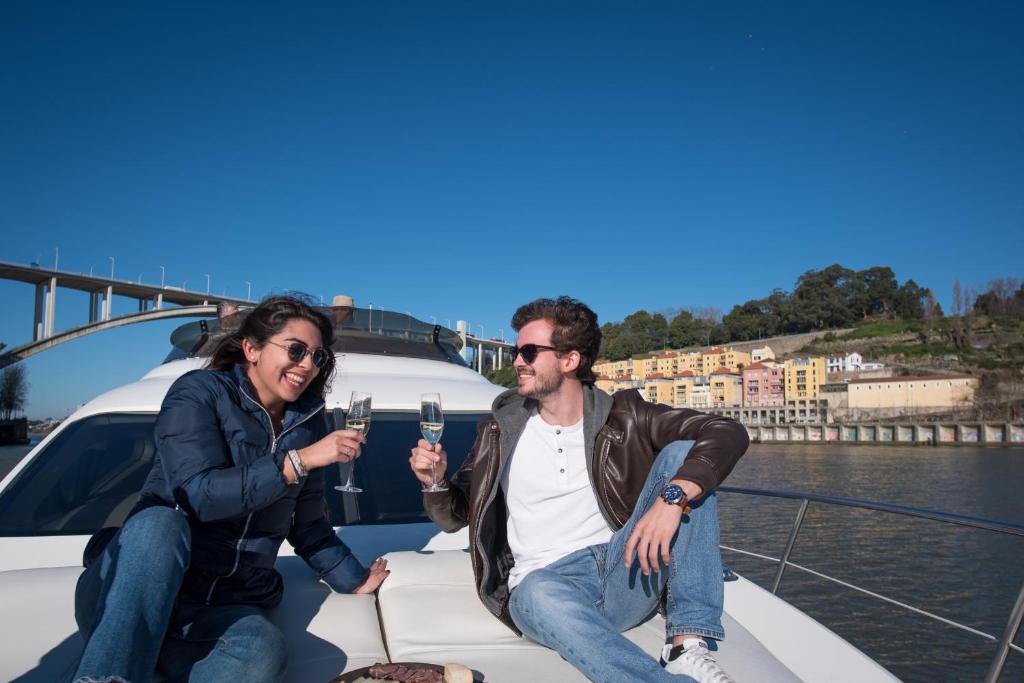 Un uomo e una donna seduti su una barca con dei bicchieri di vino di Sailing 360 Night On Board Experience a Vila Nova de Gaia