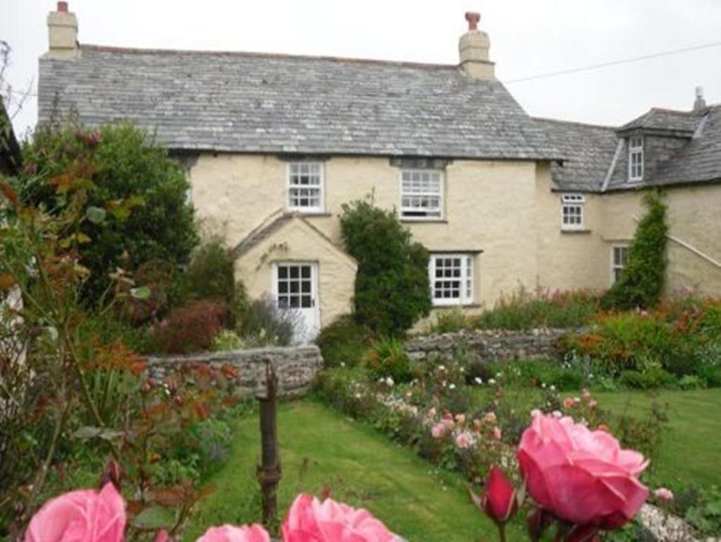 uma casa com um jardim com flores rosas em frente em Higher Tresmorn Farm em Crackington Haven