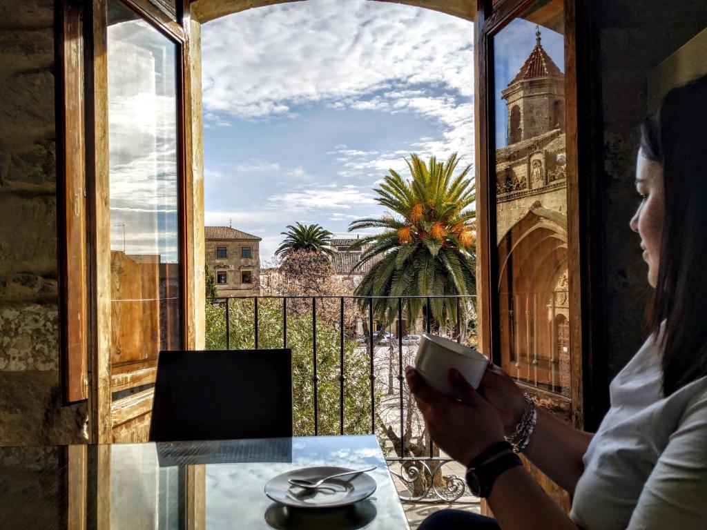 a woman looking out a window at a table with a cell phone at Apartamentos Sol de Mayo in Úbeda