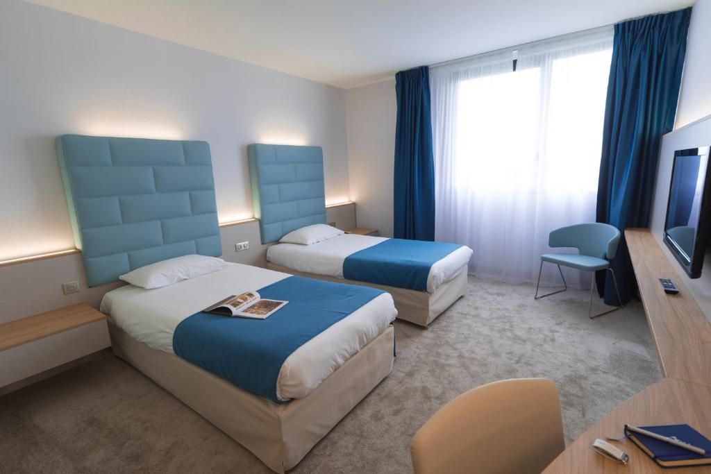 a hotel room with two beds and a television at Hotel Plaza - site du Futuroscope in Chasseneuil-du-Poitou