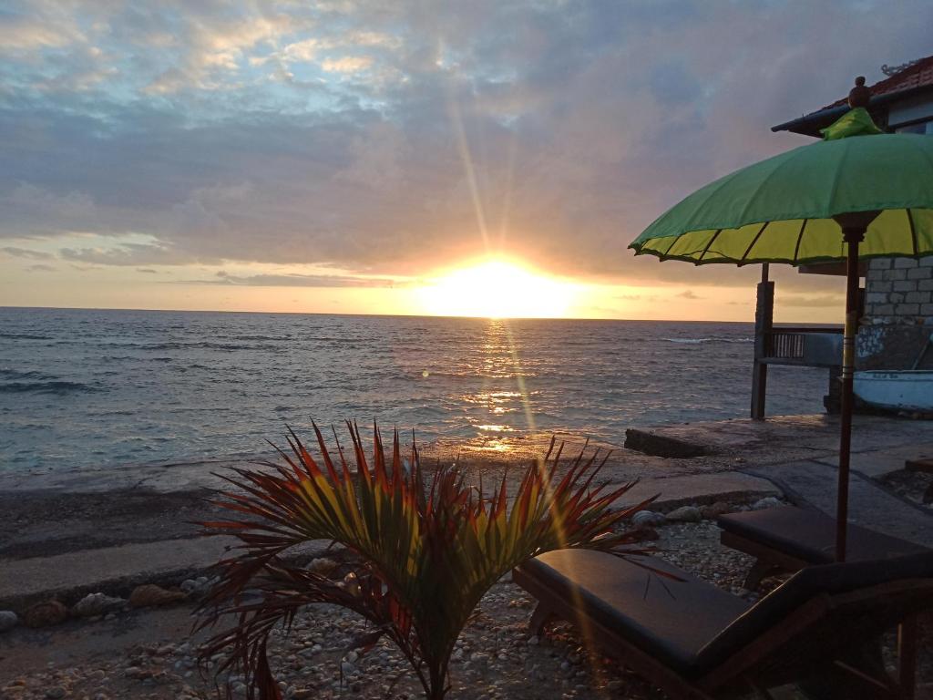a sunset on the beach with an umbrella and chairs at The Umah Prahu in Nusa Penida