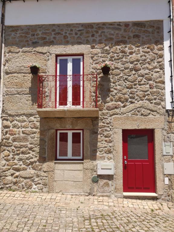 a stone building with red doors and a balcony at 3 Marias da Fonte in Lousa