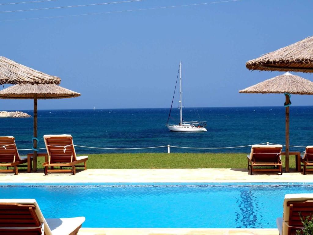 a swimming pool with chairs and a boat in the ocean at Kyparissia Blue Boutique Hotel in Kyparissia