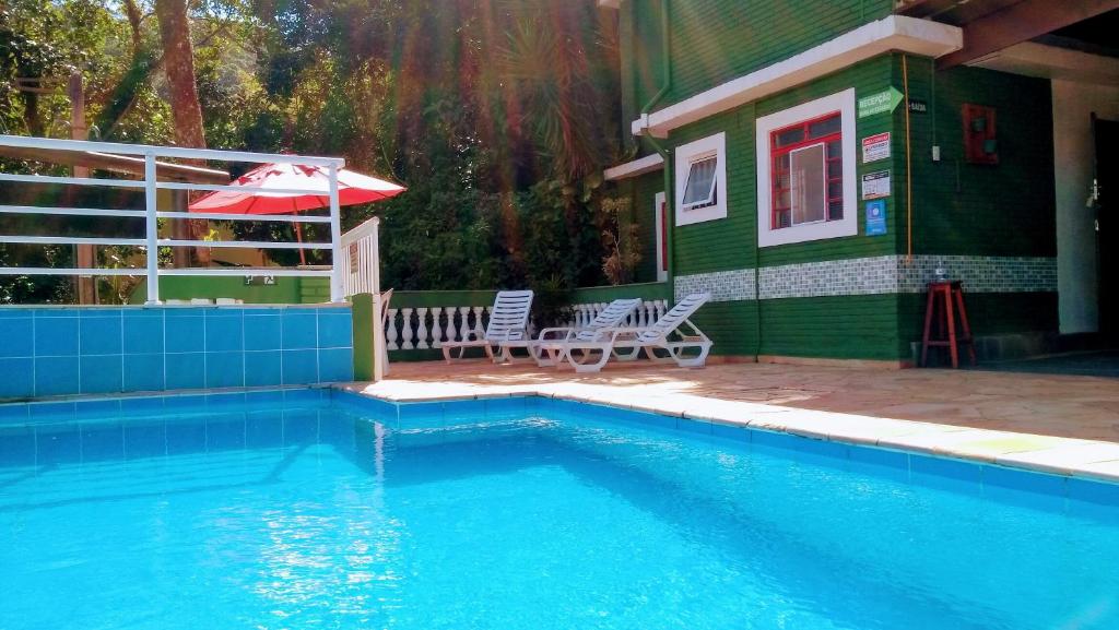 una piscina al lado de una casa con una sombrilla en Chales Virena, en Ubatuba