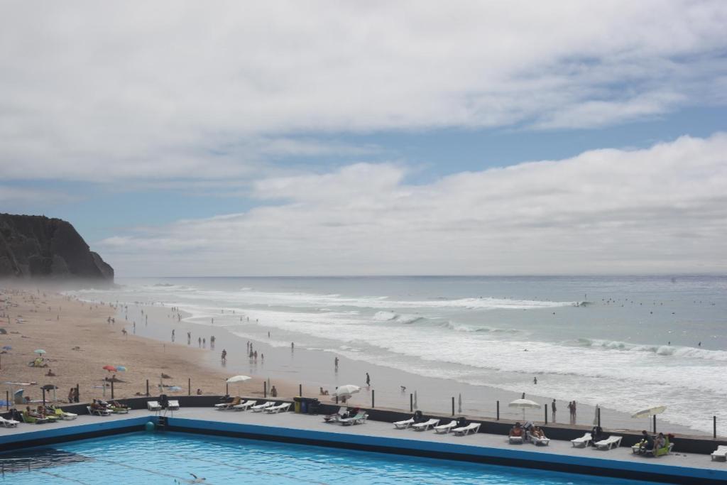 a view of a beach with a swimming pool and the ocean at ribeira dos marinheiros amarelo in Sintra