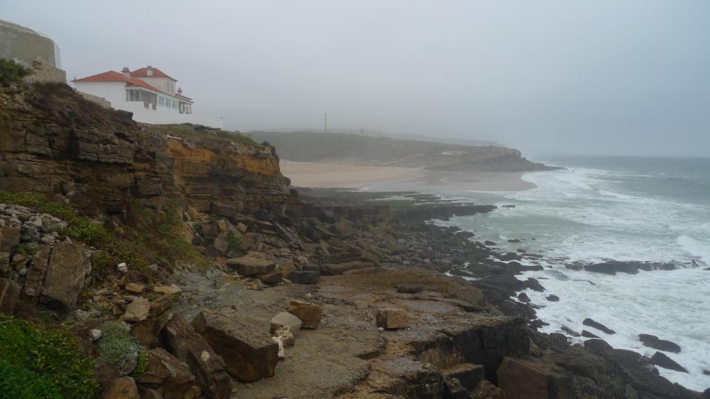 a house on top of a cliff next to the ocean at ribeira dos marinheiros amarelo in Sintra