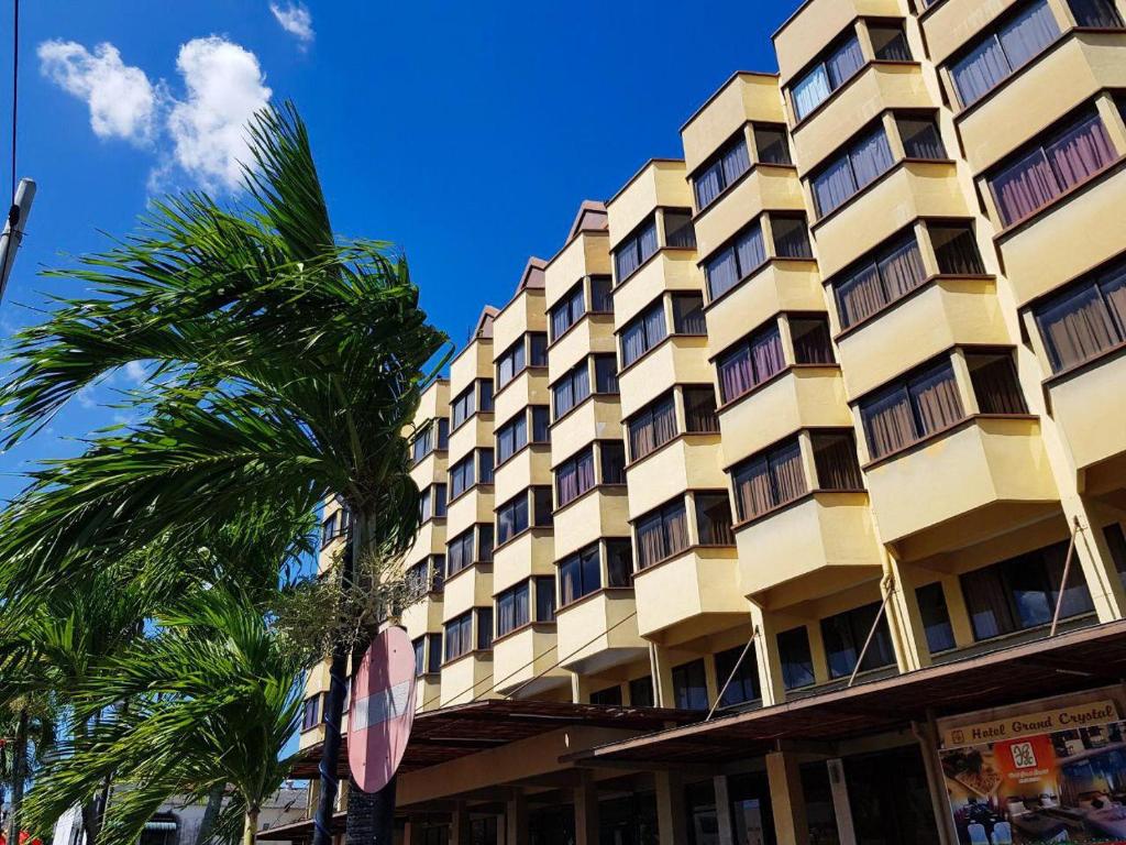 a large yellow building with palm trees in front of it at Hotel Grand Crystal in Alor Setar