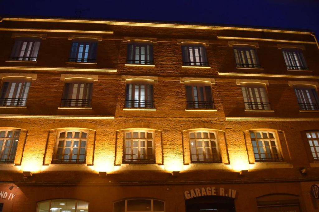 un gran edificio de ladrillo con ventanas iluminadas por la noche en Hôtel Raymond 4 Toulouse en Toulouse