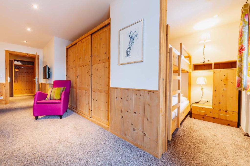 a bedroom with wooden walls and a pink chair and a bed at Hotel Aurora in Lech am Arlberg