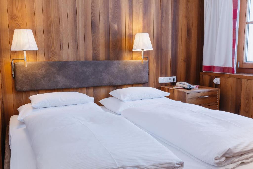 two beds in a bedroom with two lamps on a wall at Hotel Aurora in Lech am Arlberg