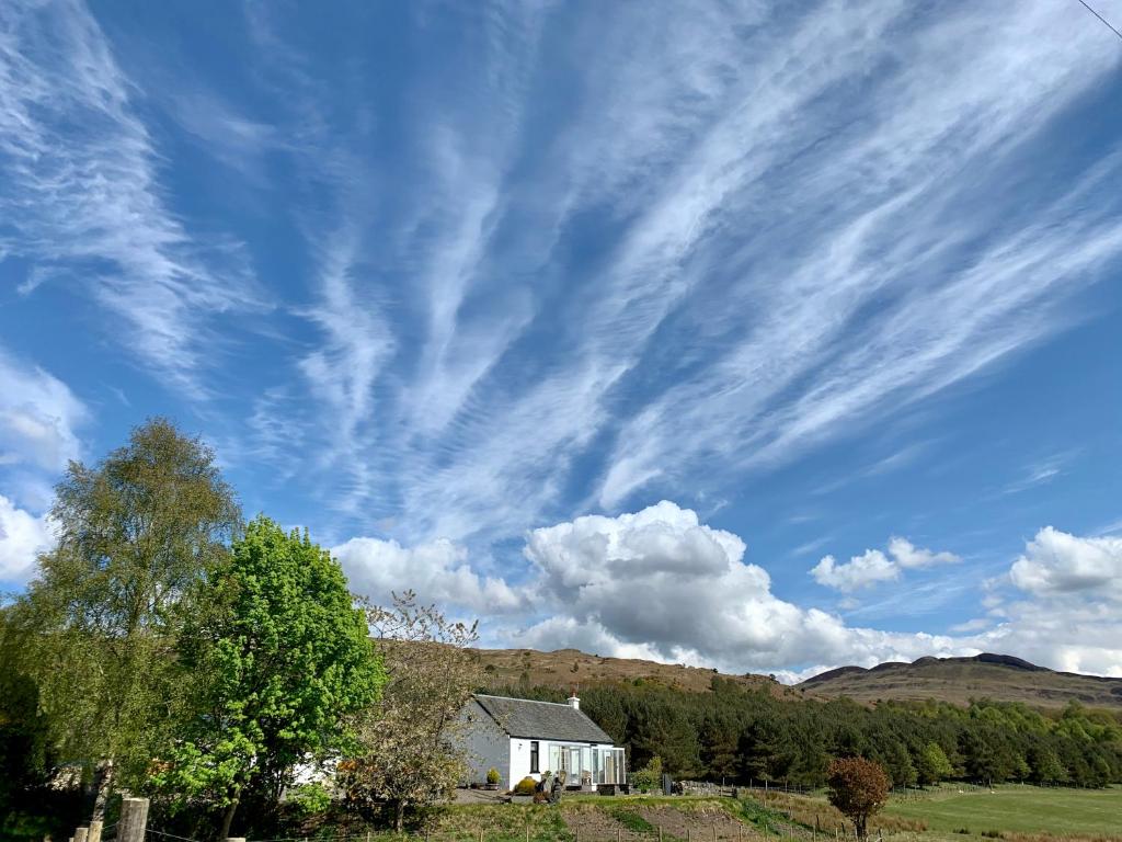 a white house in a field under a cloudy sky at Blair Cottage in Rowardennan