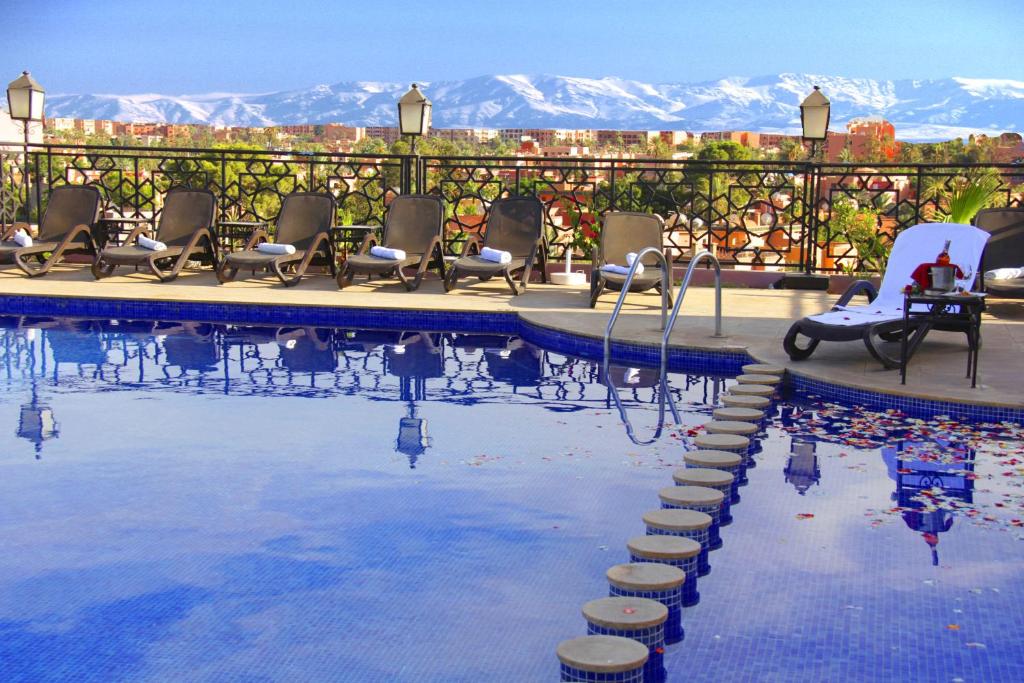a swimming pool with chairs and mountains in the background at Hotel Imperial Plaza & Spa in Marrakech